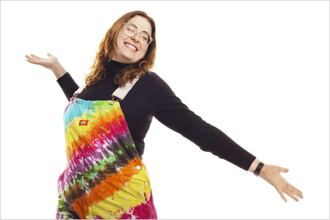 student wearing a black shirt and rainbow tie-dyed overalls.