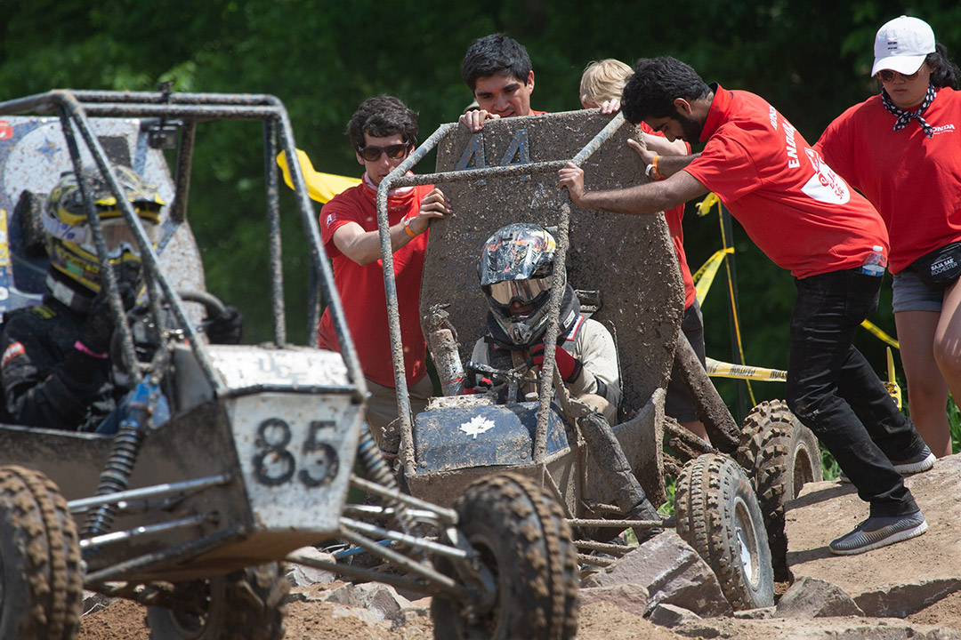 crew helping a baja car get unstuck from rocky terrain.