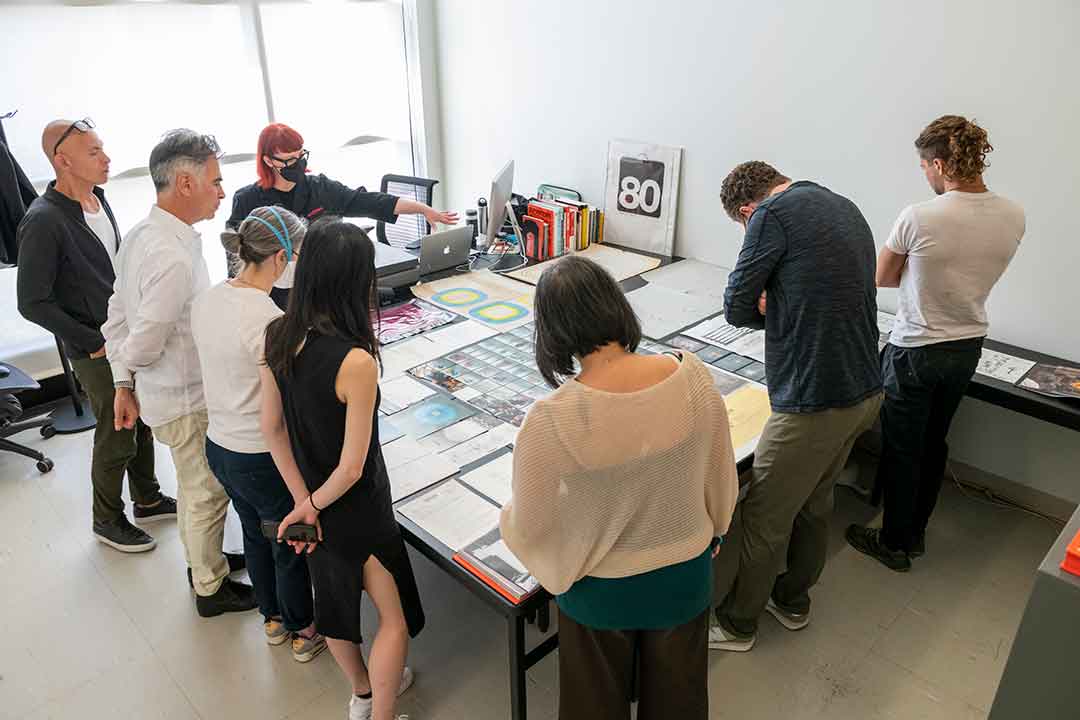 eight people standing around a table looking at samples of artwork.