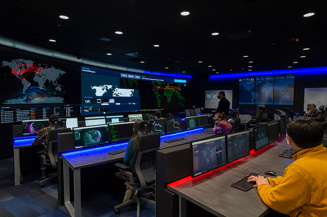 student sitting in a dark computer lab with several displays of maps of the world around the room.
