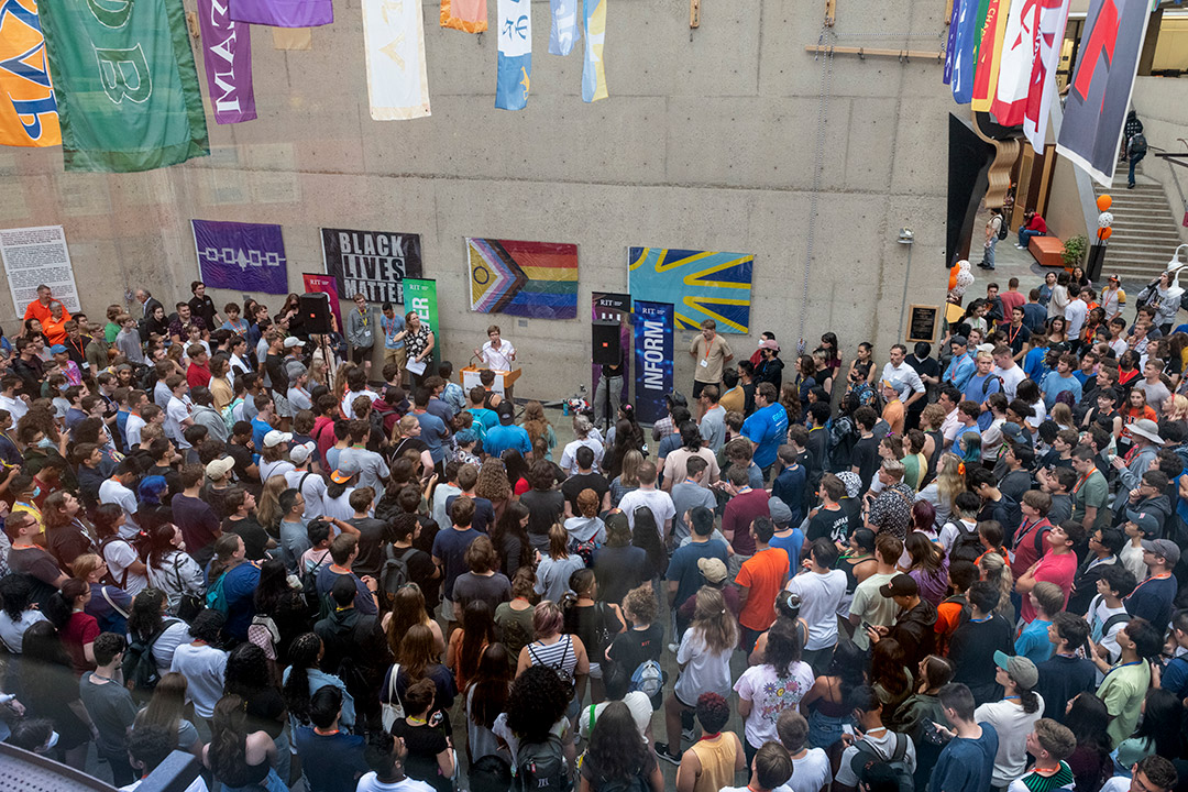 crowd of people listening to a speaker at a podium outside.