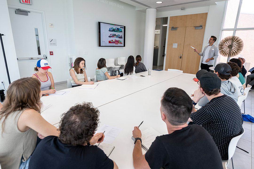 several students sitting around a rectangular table taking notes on a presentation.