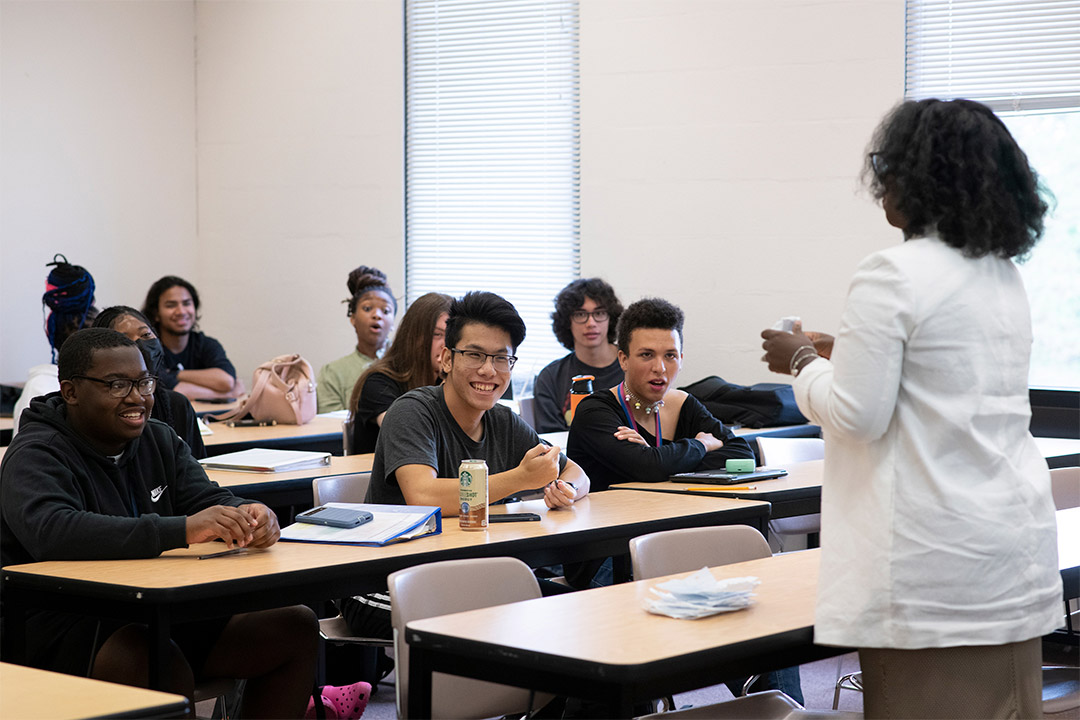 professor lecturing to students seated at long tables.