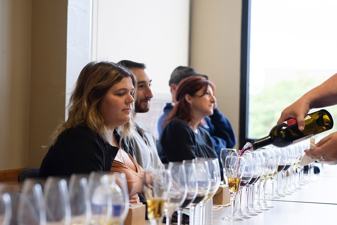 students sitting in front of a selection of wines in different shaped glasses.