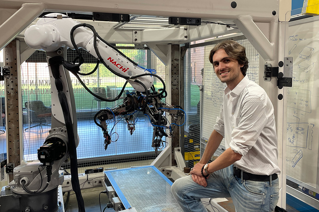 student posing next to a large, industrial 3D printer.