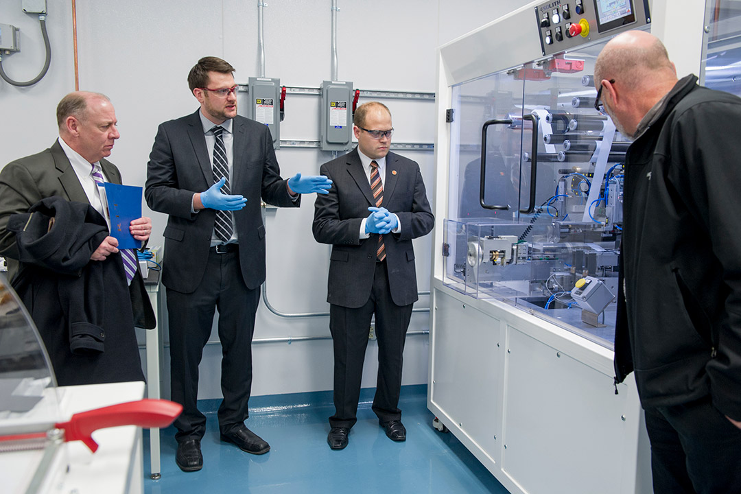 four people in suits looking at machinery in a case.