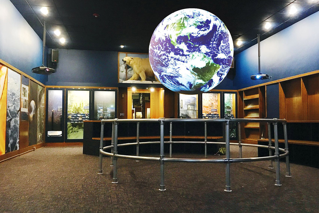a science museum exhibit featuring projections of the surface of the Earth on a large sphere.