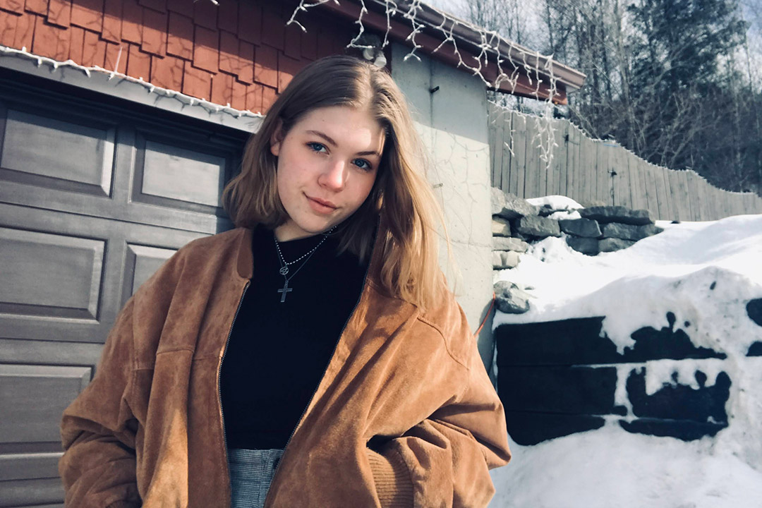 student standing outdoors near a house with snow in the background.