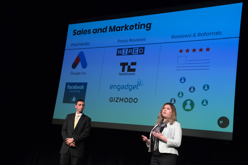 two people giving a presentation in front of a large screen.