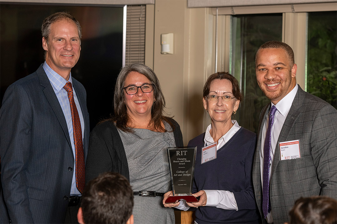 four people standing with one holding an award.