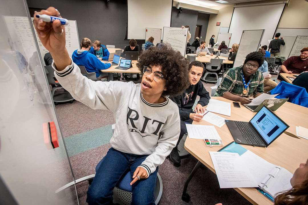 students sitting at a table and writing on a dry-erase board.