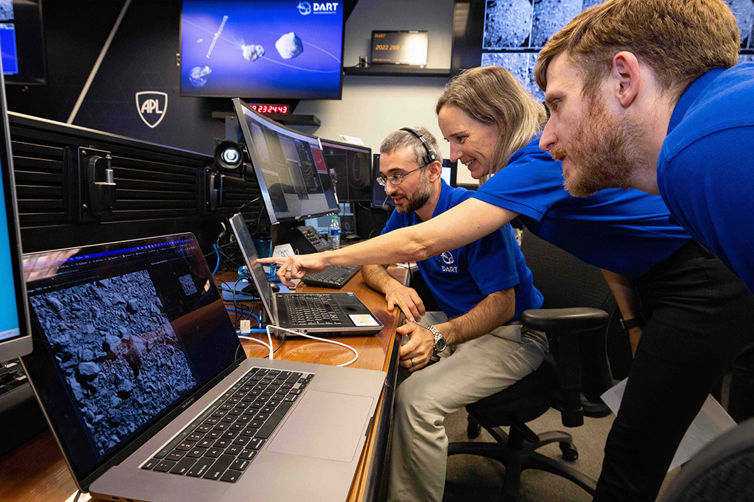 three scientists looking and pointing at a series of laptops.