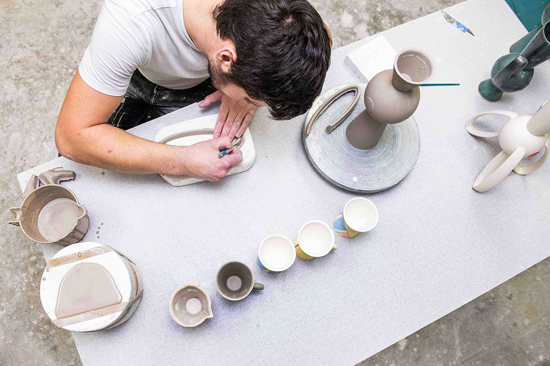 Artists hands cutting clay with tool.