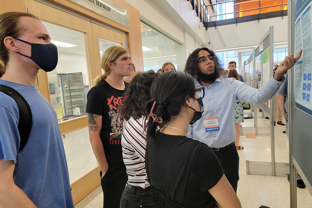 student giving poster presentation to other students.