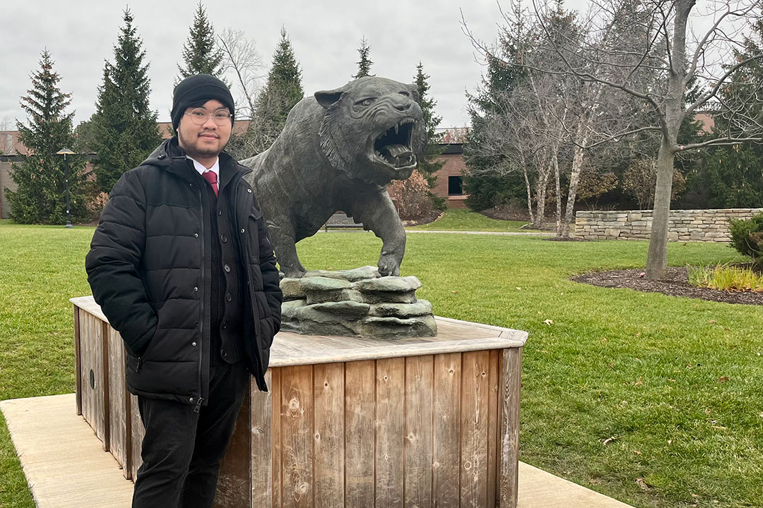 Photo of Colin Vo next to the Tiger shrine on RIT's campus