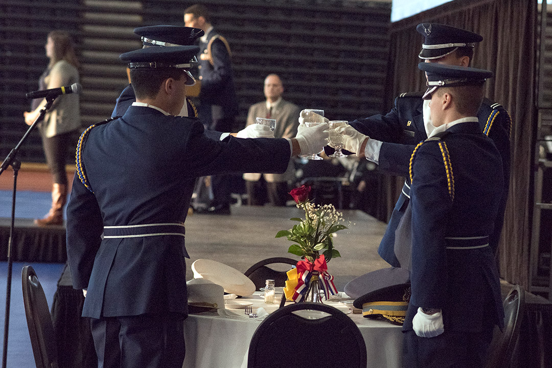 four people dressed in military dress uniform hold water glasses at a dinner table.