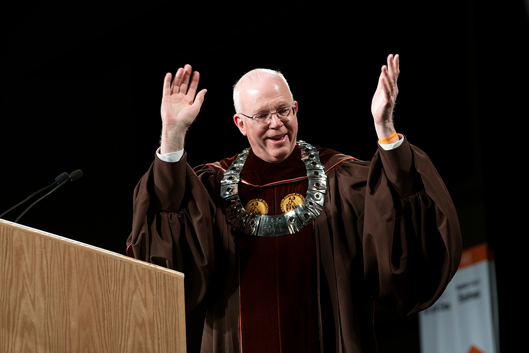 RIT President Munson wearing convocation ceremonial robes and holding his hands in the air.
