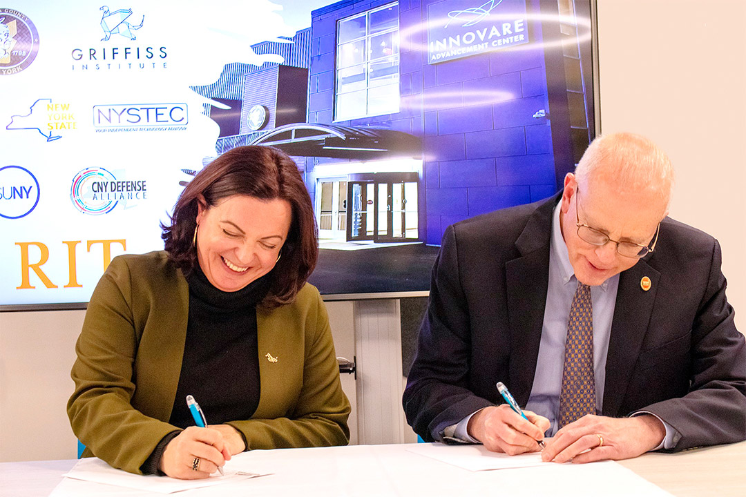 two people sitting at a table signing documents.