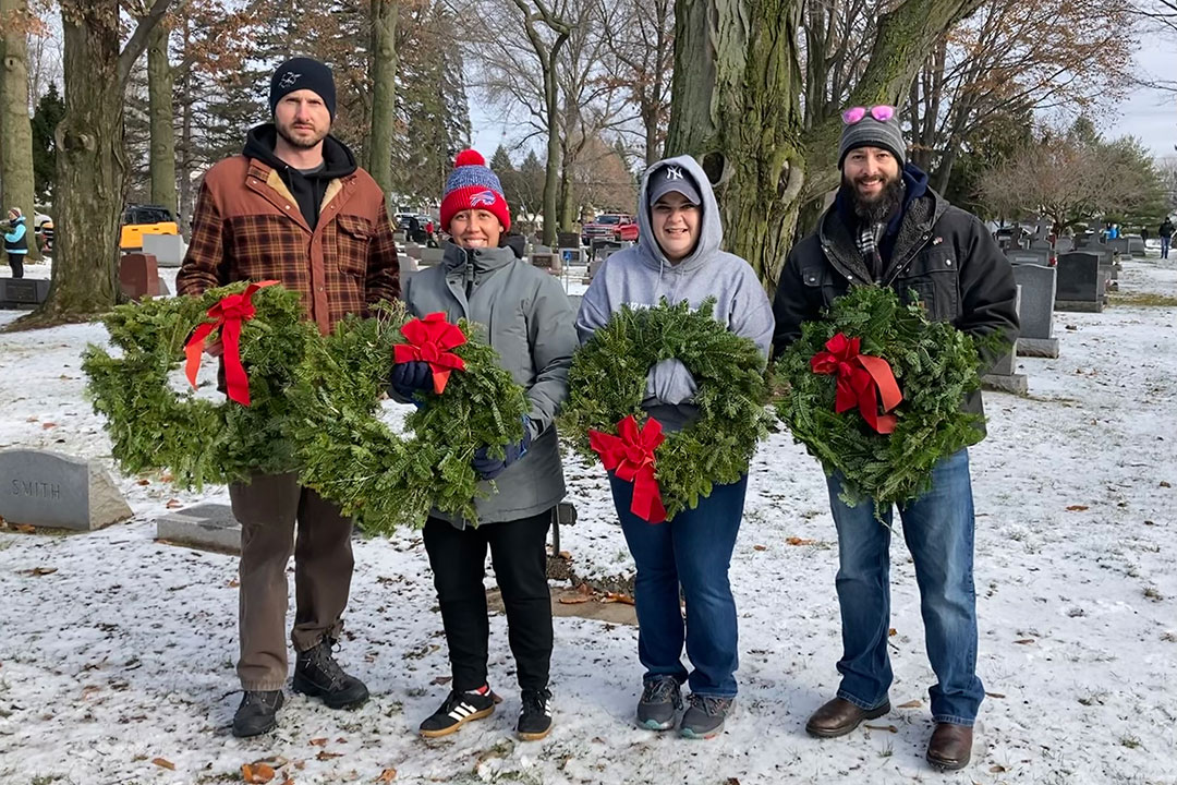 Two RIT staff members and two members of the Veteran Students Club on campus post for a photo with wreaths for Wreaths Across America Day