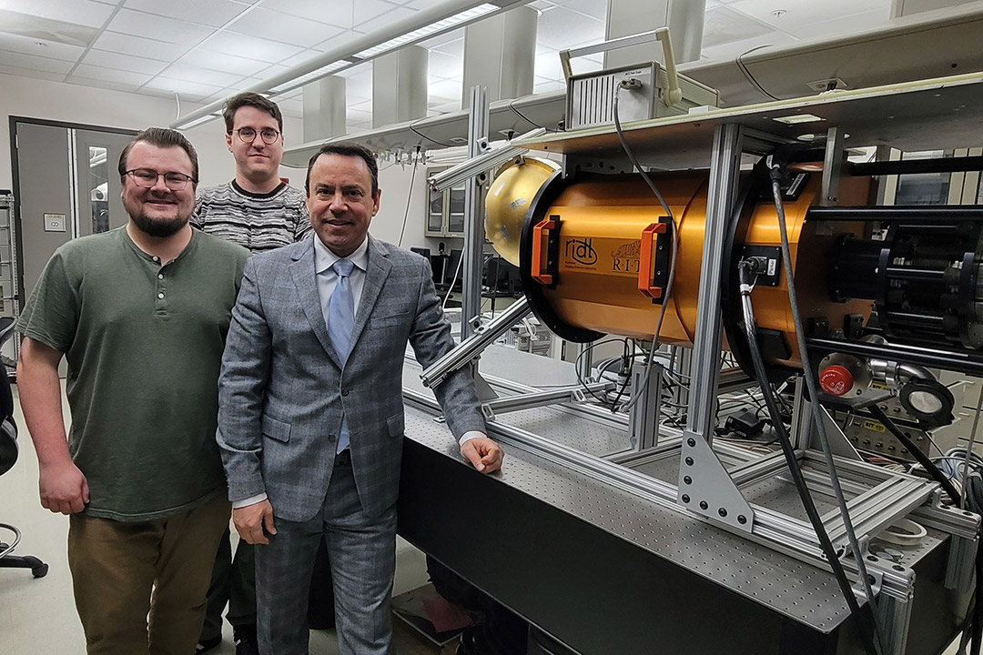 three people standing next to a telescope in a lab.