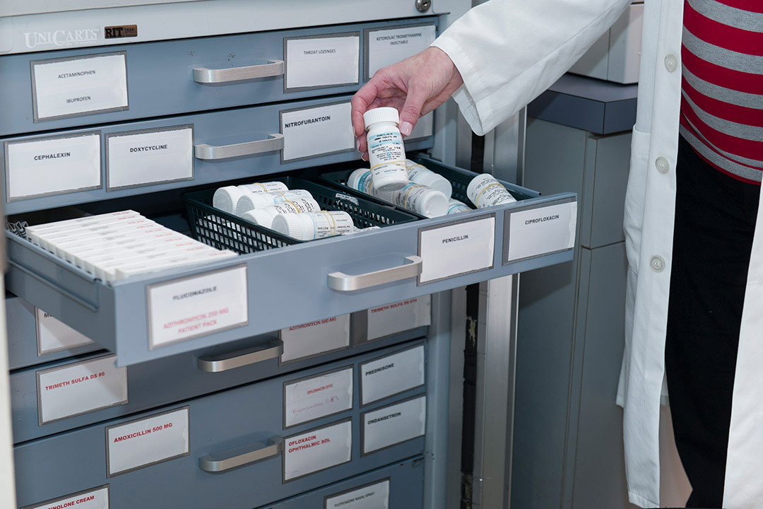 person holding a bottle of prescription medication from an open drawer of medicine boxes and bottles.