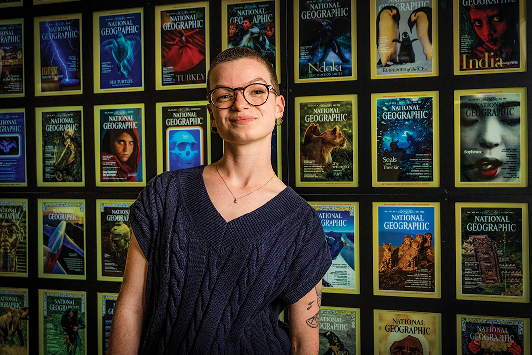 college student posing in front of a wall of National Geographic magazine covers.