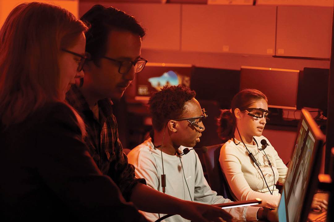 students wearing eyewear and microphones along with faculty members looking at computer screens.