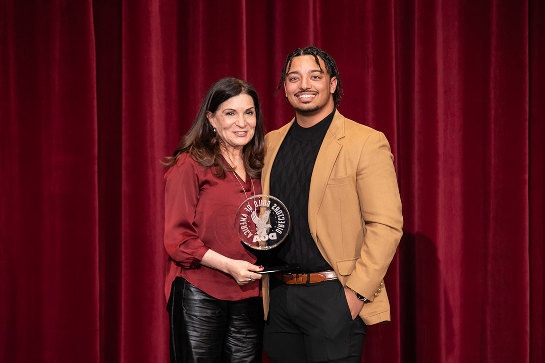 two people standing in front of a red curtain holding a glass award.