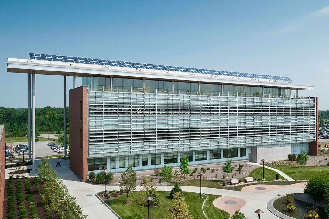 exterior of a multistory building with a wall of glass windows and solar panels on the roof.