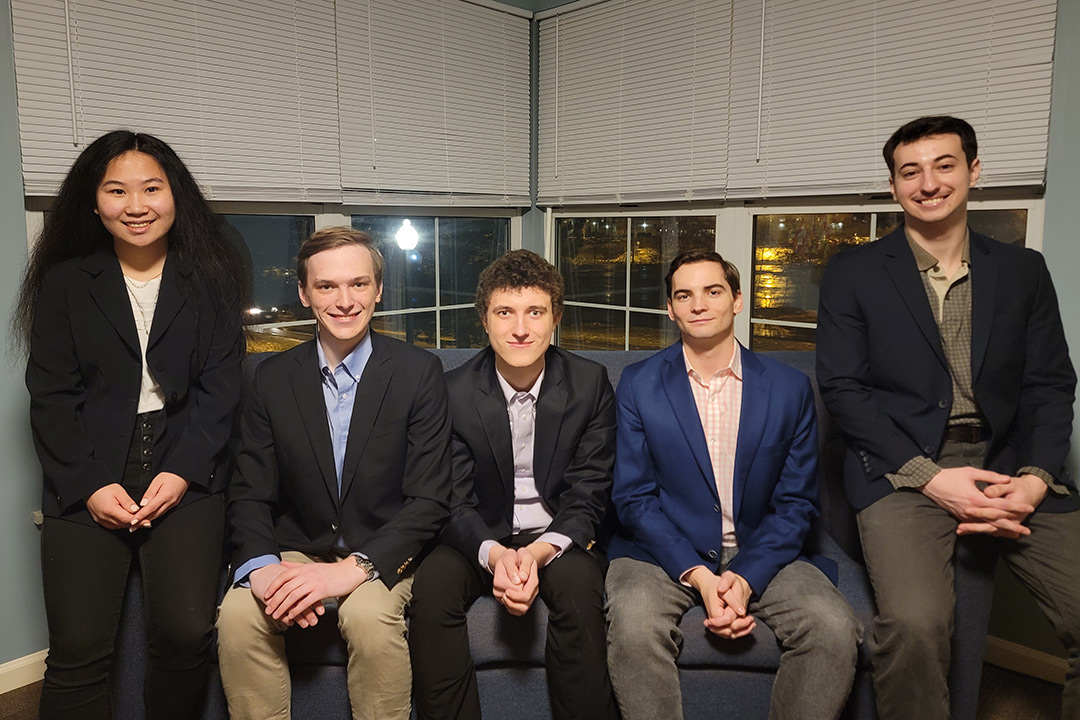 five college students sitting on a couch wearing business attire.
