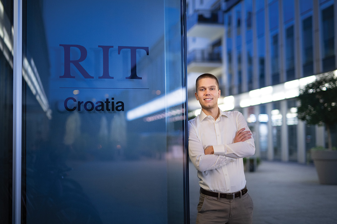 college student leaning against a glass sign for RIT Croatia.