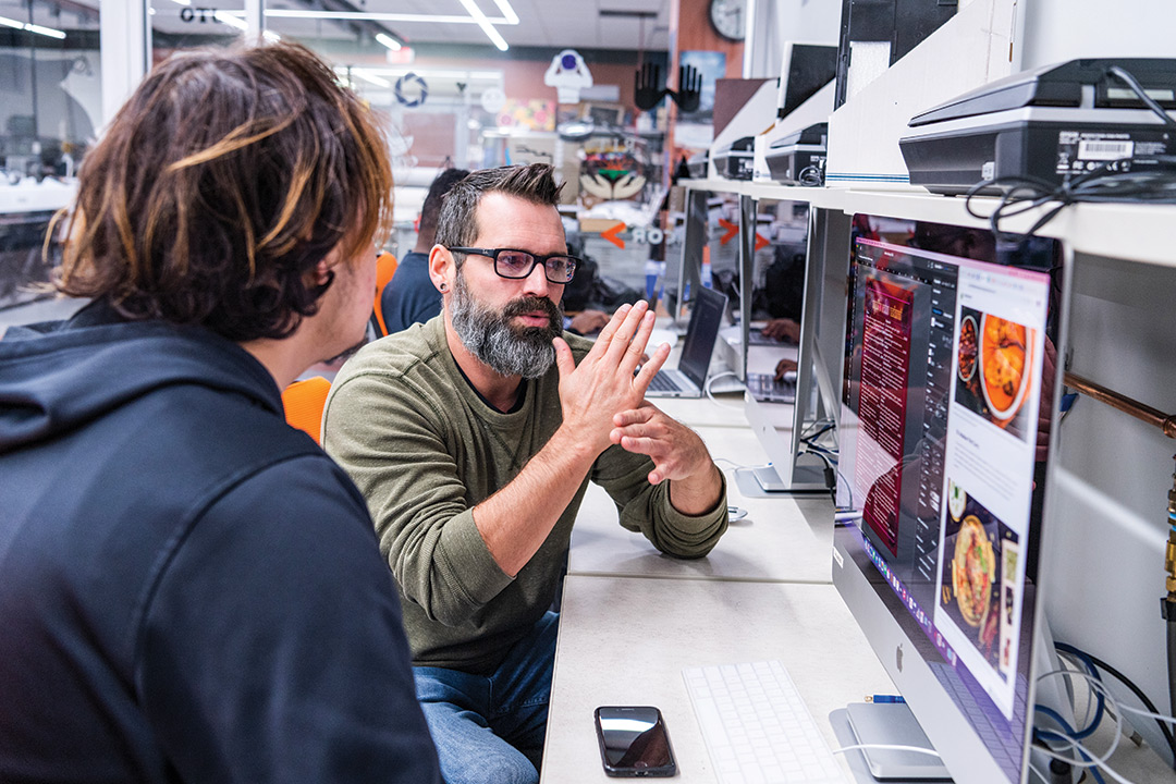 professor using sign language and sitting with a student in front of a computer.