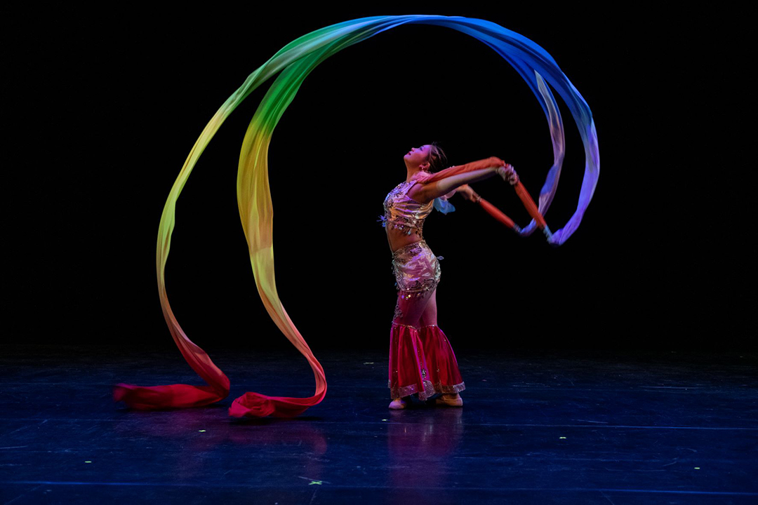 Kaitlyn Moy performing on stage with two rainbow colored ribbons.