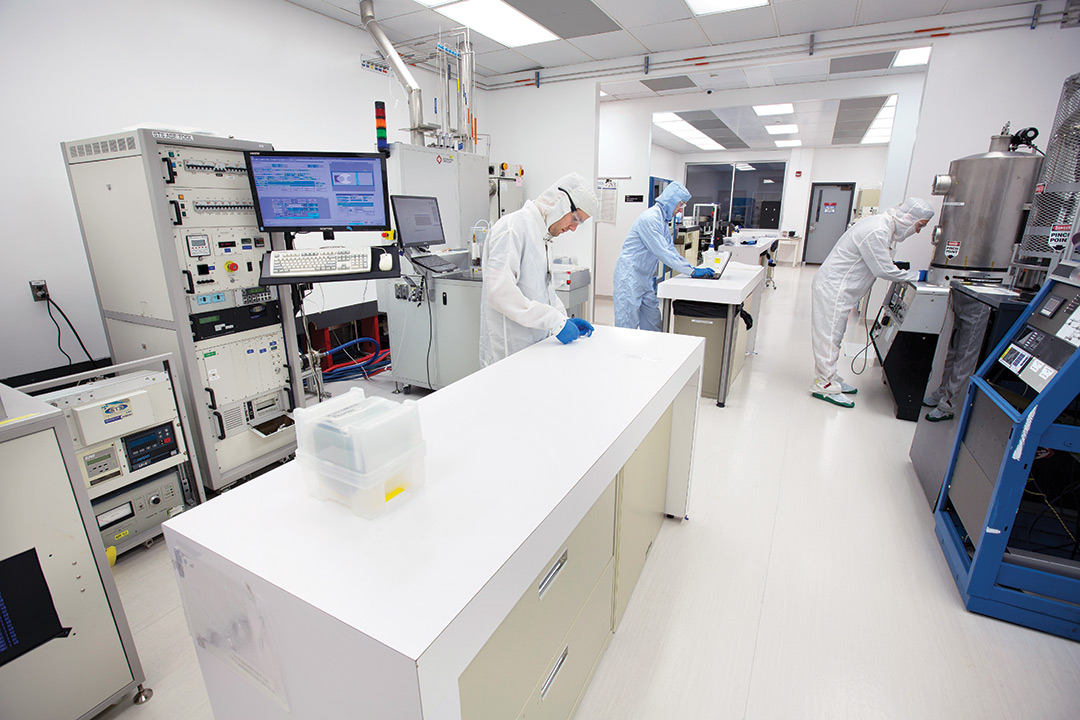 three researchers wearing clean suits working in a cleanroom.