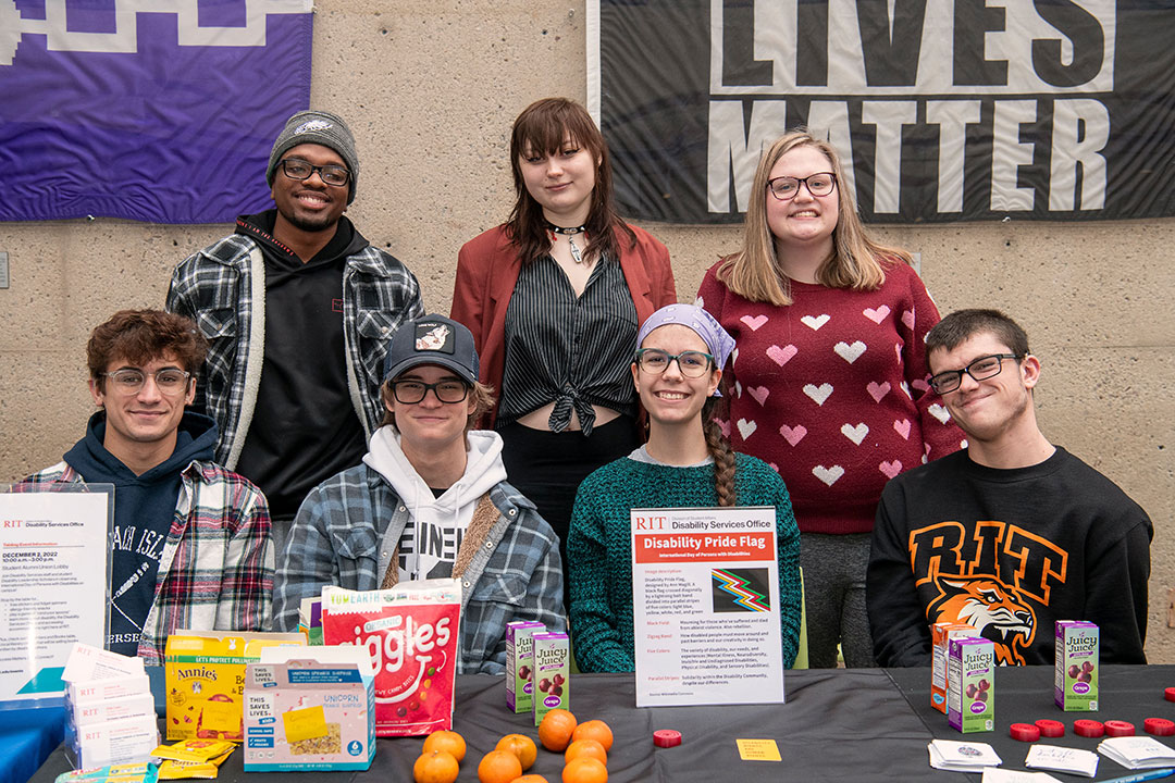 three students standing and four students seated at an information table about disabilities.