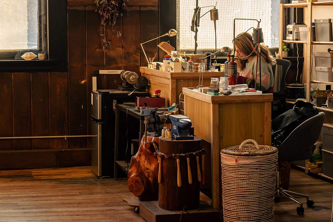 person working in a studio surrounded by metalworking tools and supplies.