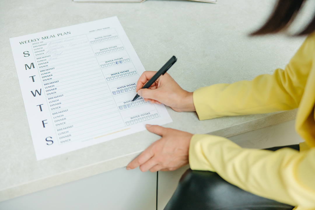 person filling out a weekly meal plan worksheet.