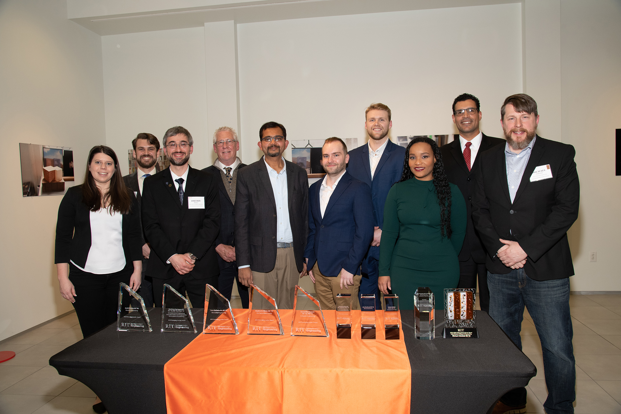 Ten people standing behind a table with a black and orange tablecloth and crystal awards on it. The people are smiling and looking at the camera.