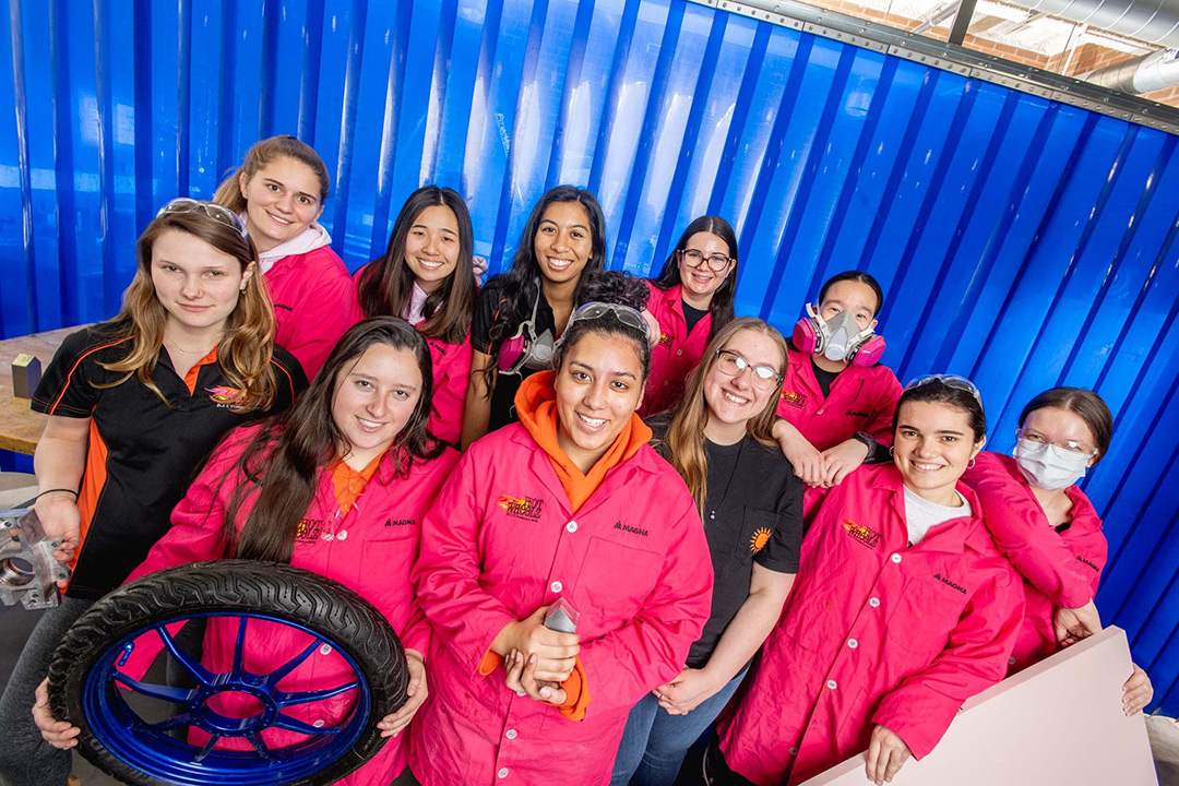 group of eleven college students holding components to an electric car.