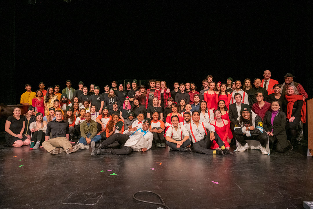 'group of more than 70 performers posing for a group photo on a stage.'