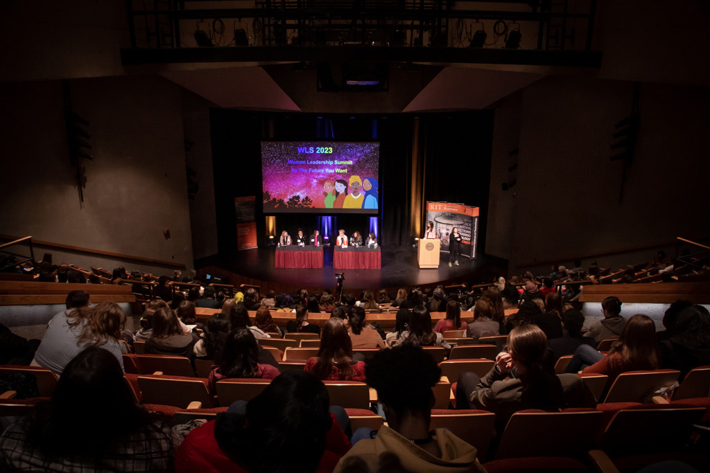 view of a stage with panelists from the back of an auditorium.