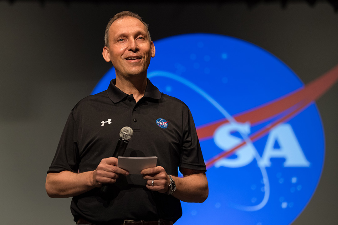 man speaking in front of a NASA logo.