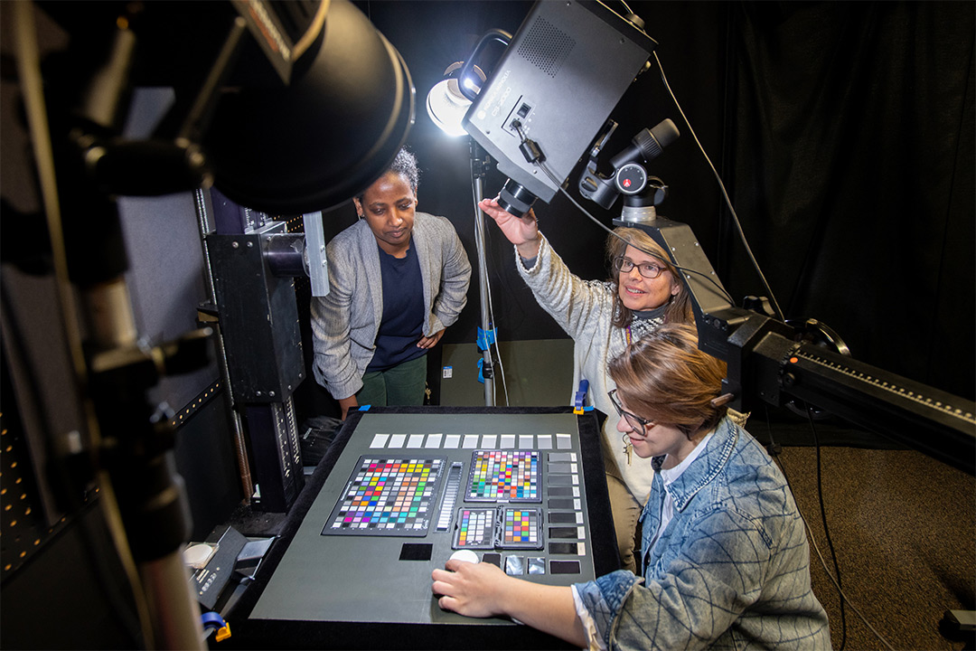 three researchers lining up color samples on a machine with a camera.