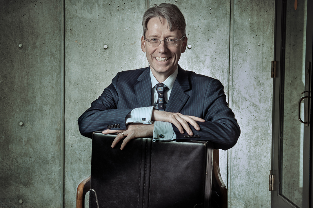 Person sitting in a chair, in a suit, with a briefcase on their lap.