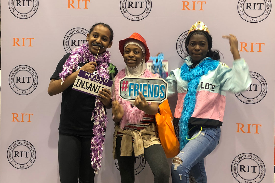 Three youth pose next to RIT backdrop during a past Imagine RIT event