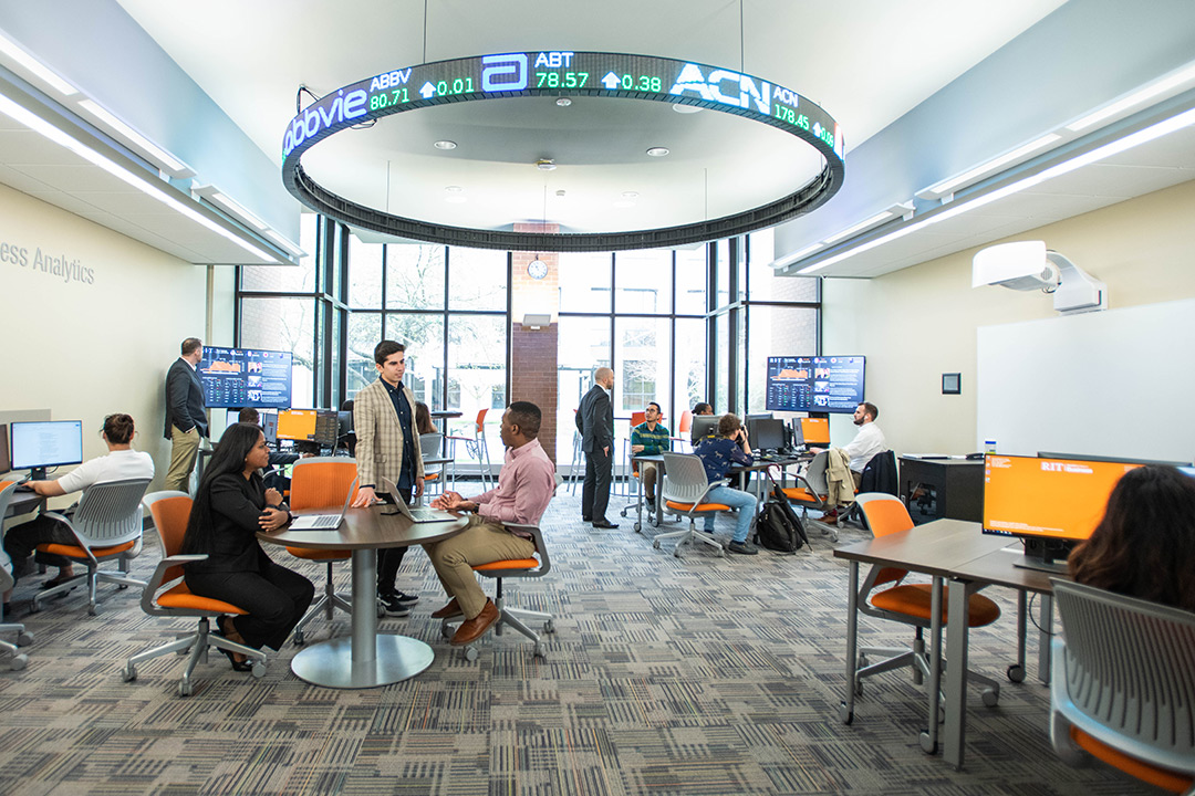 business college students working in a room with a large, round, digital stock ticker.