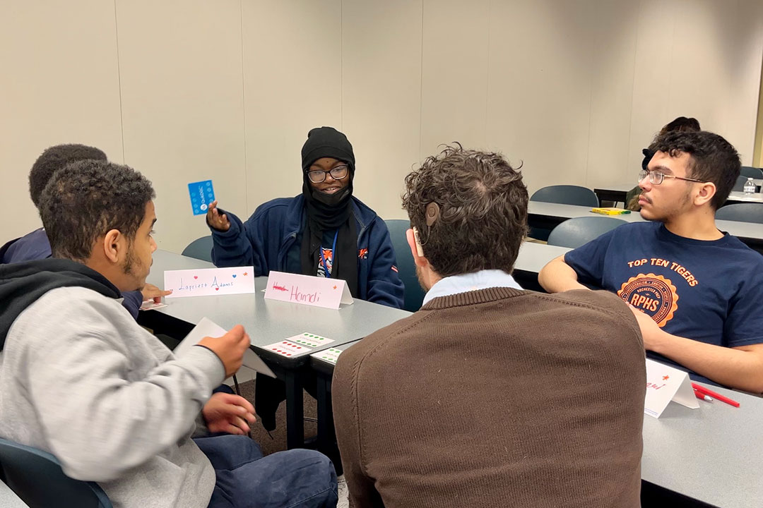 Five students sitting around a table taking to each other