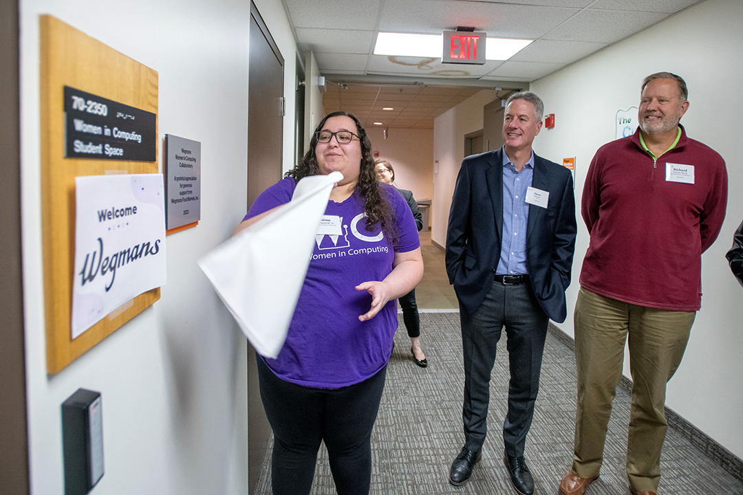 Three people standing looking at new sign by door for Women in Computing Collaboratory.