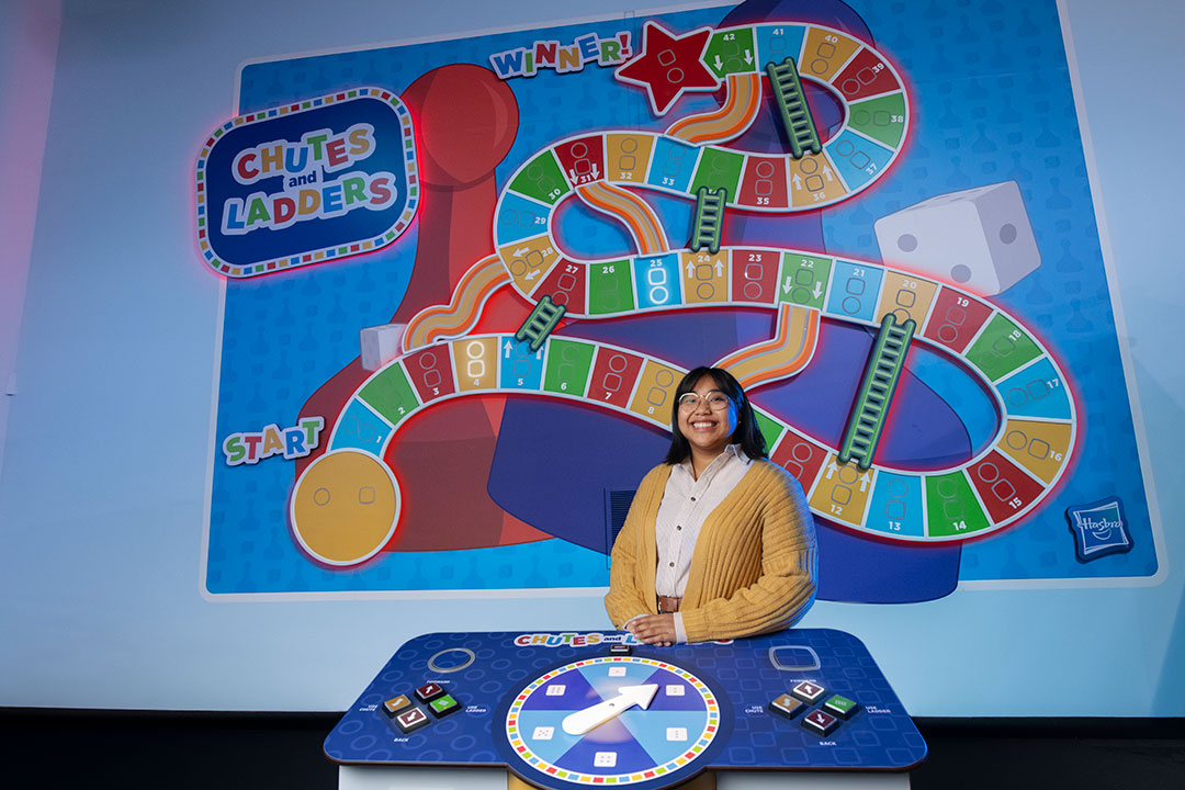 a college student standing in front of a large display of the Chutes and Ladders board game.