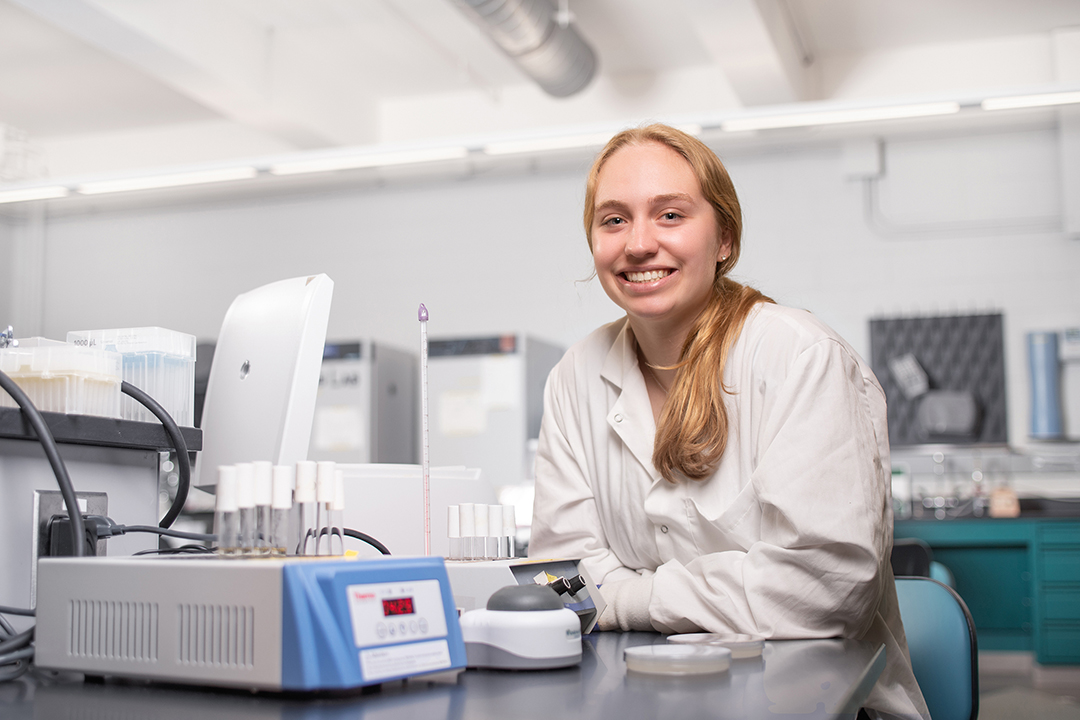 Person in white coat sitting at a lab desk.